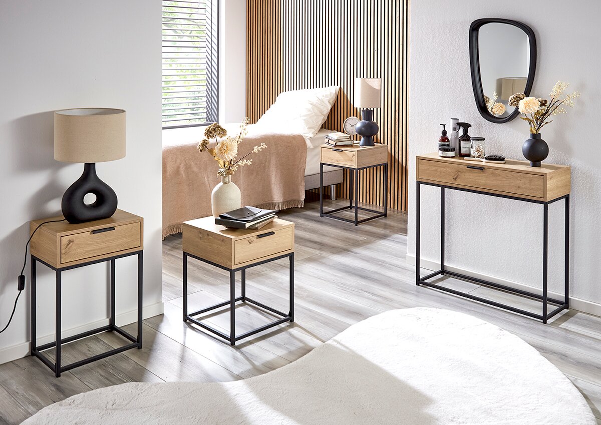 Modernes Schlafzimmer-Setting mit Konsolentisch und zwei Beistelltischen aus hellem Holz auf schwarzem Metallgestell, dekoriert mit Lampen, Vasen und Spiegel; Perspektive: frontale, leicht seitliche Raumansicht auf Augenhöhe.