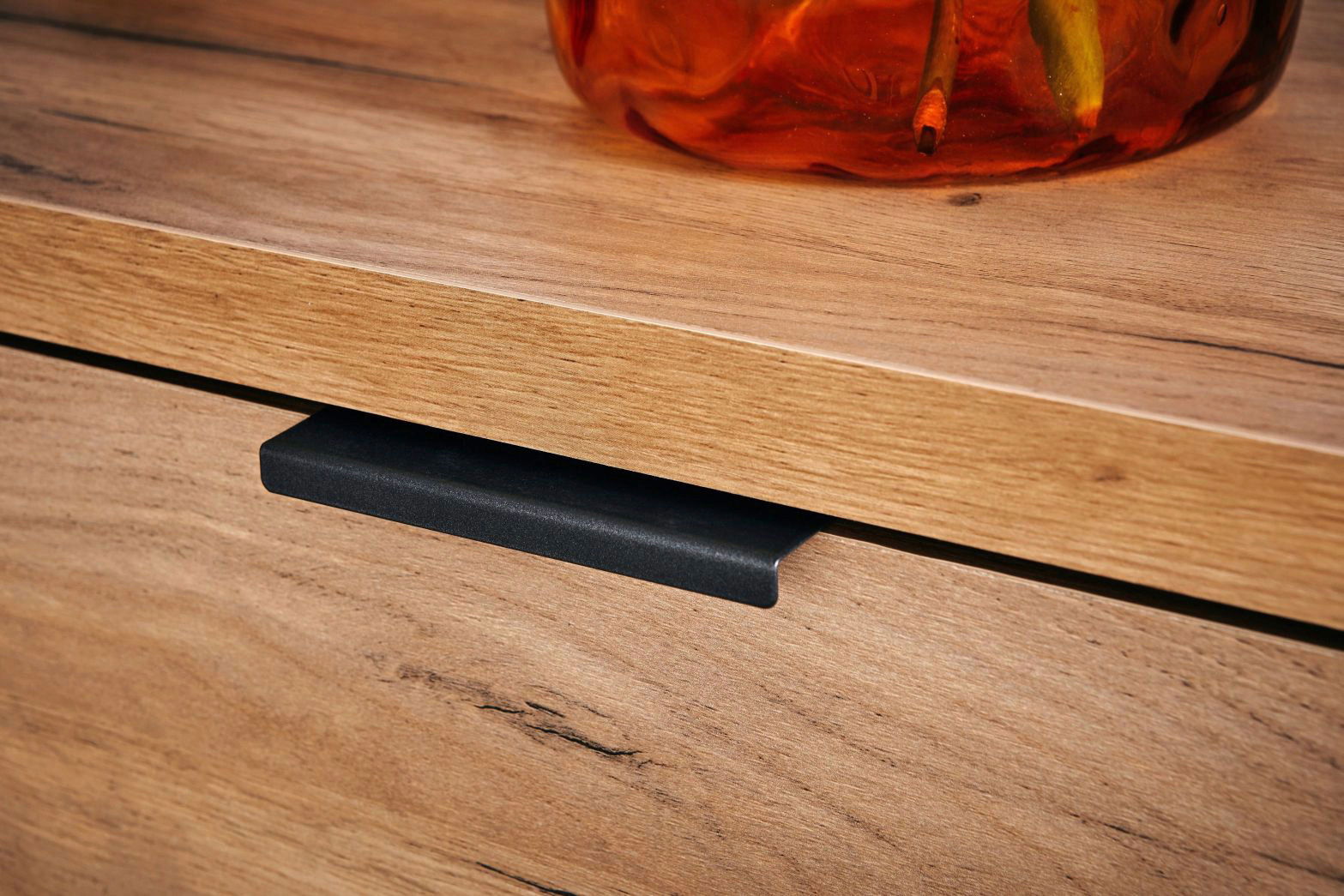 Nahaufnahme eines Eck-Schreibtischs aus Holz mit einer schwarzen Griffleiste und einem dekorativen Element auf der Oberfläche.