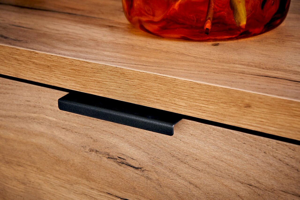 Nahaufnahme eines Eck-Schreibtischs aus Holz mit einer schwarzen Griffleiste und einem dekorativen Element auf der Oberfläche.