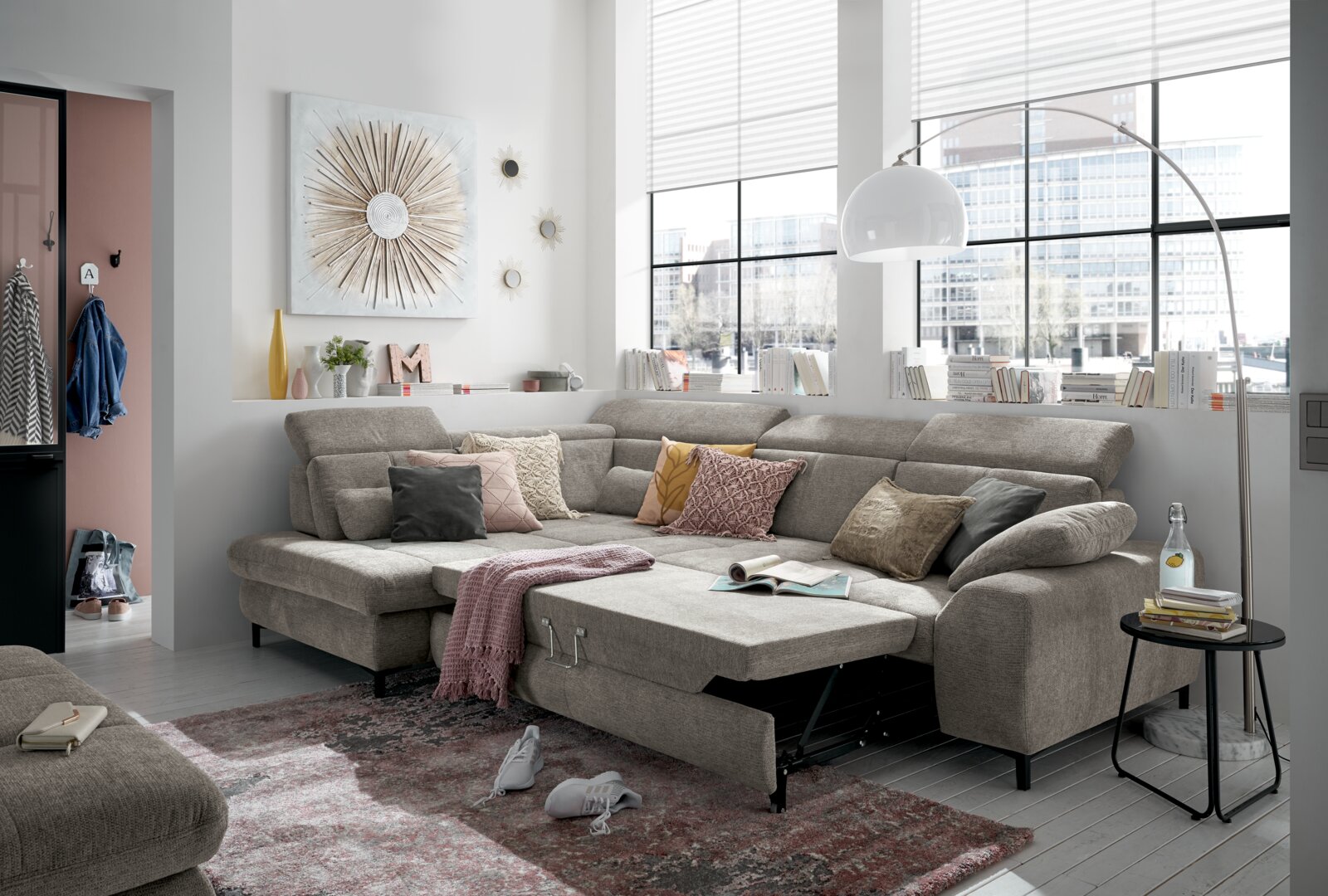 Een gezellige hoekbank in een moderne woonkamer, met een grijze stoffen bekleding en diverse kussens, gefotografeerd vanuit een vooraanzicht.