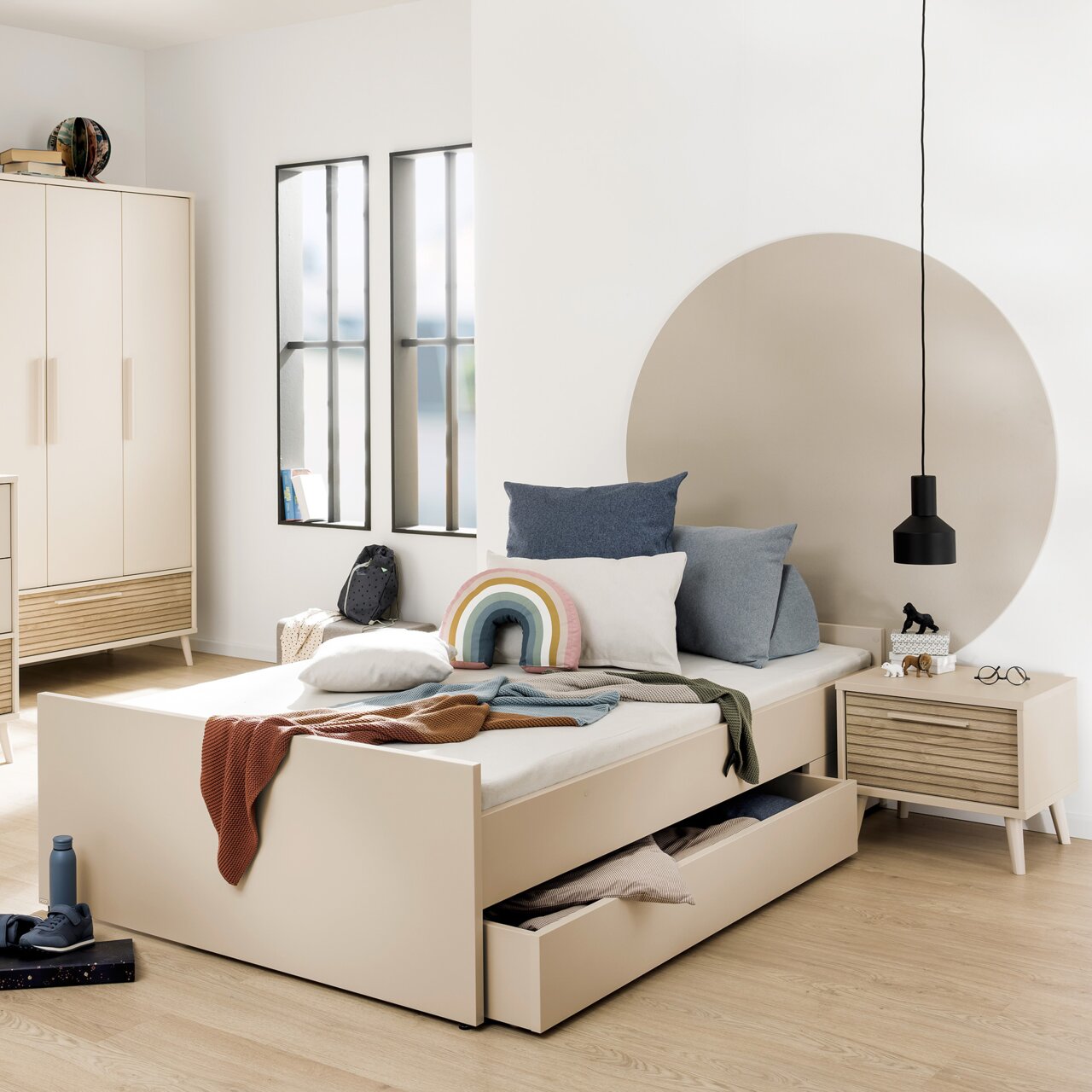 Modernes Schlafzimmer mit großem Bettkasten in hellem Holz, seitliche Perspektive. Der Bettkasten ist teilweise geöffnet und zeigt Stauraum. Dekoriert mit Kissen und Decken in sanften Farben.