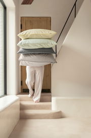 Person trägt einen Stapel gestreifter Kissenbezüge in verschiedenen Farben eine Treppe hinauf, seitliche Perspektive.