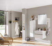 Moderner Badezimmer-Mittelschrank in Weiß, links an der Wand montiert, mit dekorativen Elementen darauf, seitliche Perspektive.