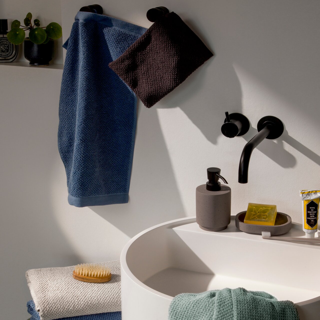 Badezimmer mit Handtüchern in verschiedenen Farben, aufgehängt an schwarzen Haken, mit Waschbecken und Seifenspender, seitliche Perspektive.