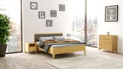 Modernes Schlafzimmer mit einem Holzbett, Nachttisch und Kommode in einem hellen Raum mit großen Fenstern, seitliche Perspektive.