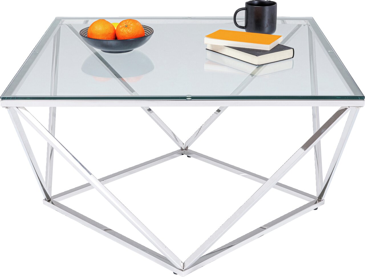 Moderne salontafel met glazen blad en geometrisch metalen onderstel, gefotografeerd vanuit een schuine hoek aan de voorkant. Op de tafel staan een schaal met sinaasappels, twee boeken en een zwarte kop.