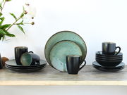 Kombiservice Jawa 16-tlg. in stilvollem Design mit schwarzer Außenseite und türkisfarbener Innenseite, bestehend aus Tellern und Tassen, auf einem Holztisch arrangiert. Frontalansicht.