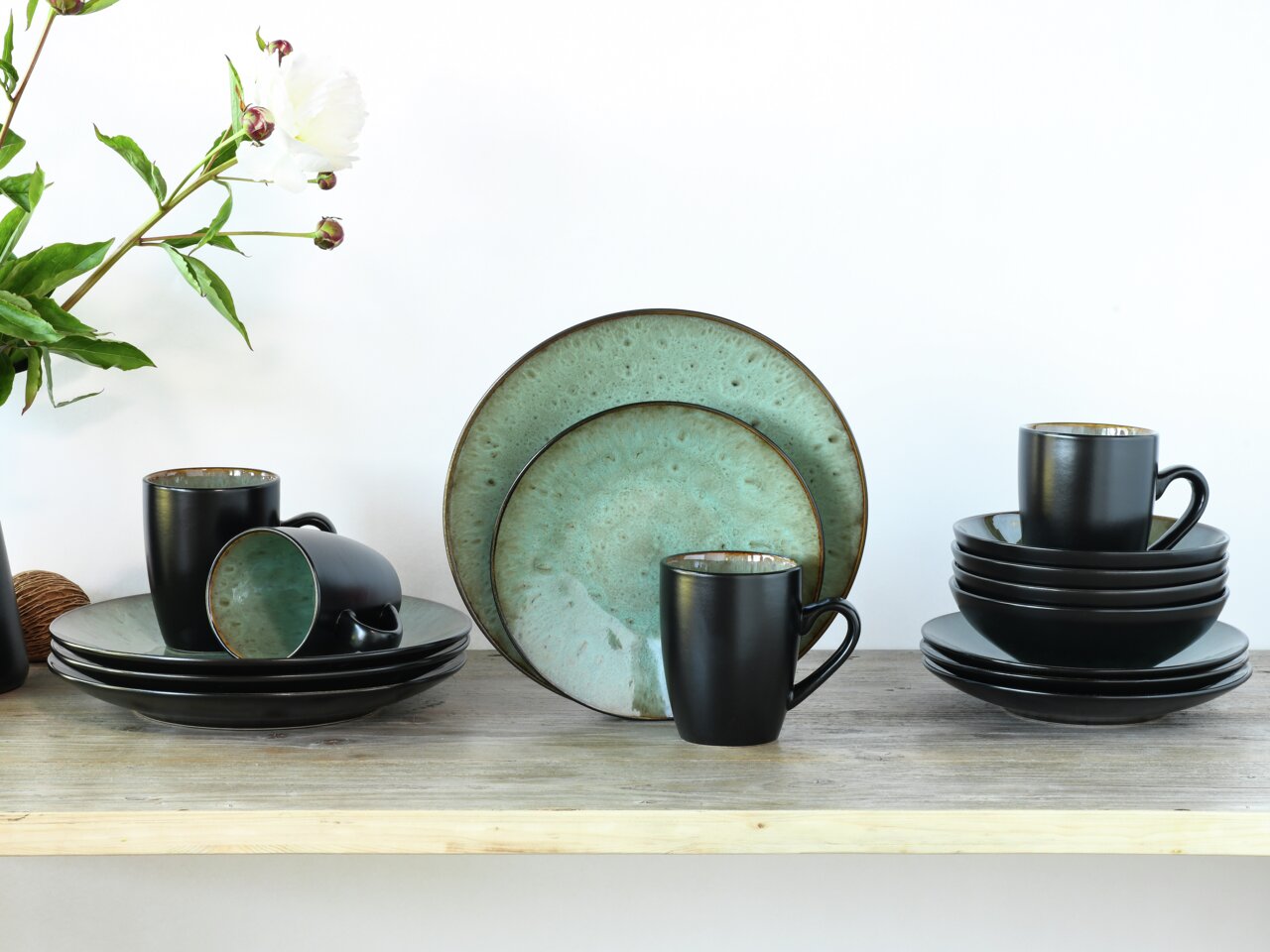 Kombiservice Jawa 16-tlg. in stilvollem Design mit schwarzer Außenseite und türkisfarbener Innenseite, bestehend aus Tellern und Tassen, auf einem Holztisch arrangiert. Frontalansicht.