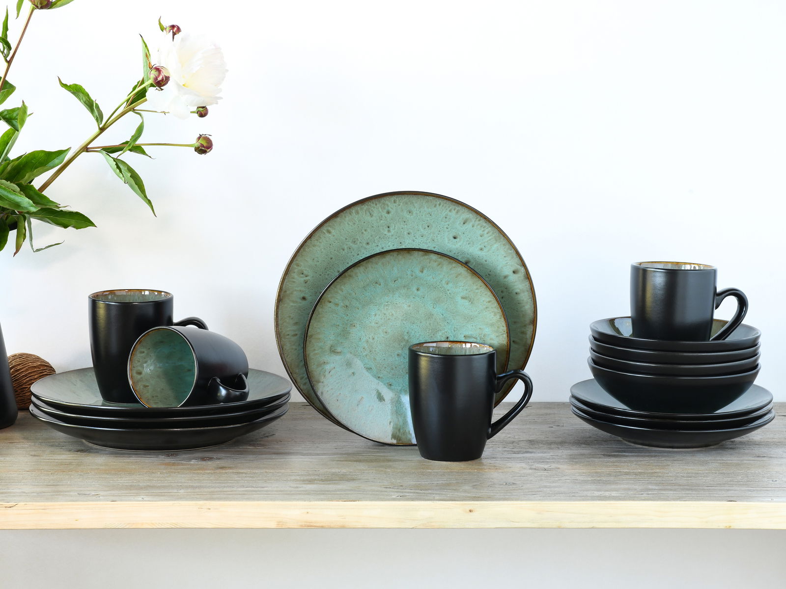 Kombiservice Jawa 16-tlg. in stilvollem Design mit schwarzer Außenseite und türkisfarbener Innenseite, bestehend aus Tellern und Tassen, auf einem Holztisch arrangiert. Frontalansicht.