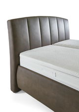 Nahaufnahme eines Polsterbetts mit braunem Kopfteil und weißer Matratze, seitliche Perspektive