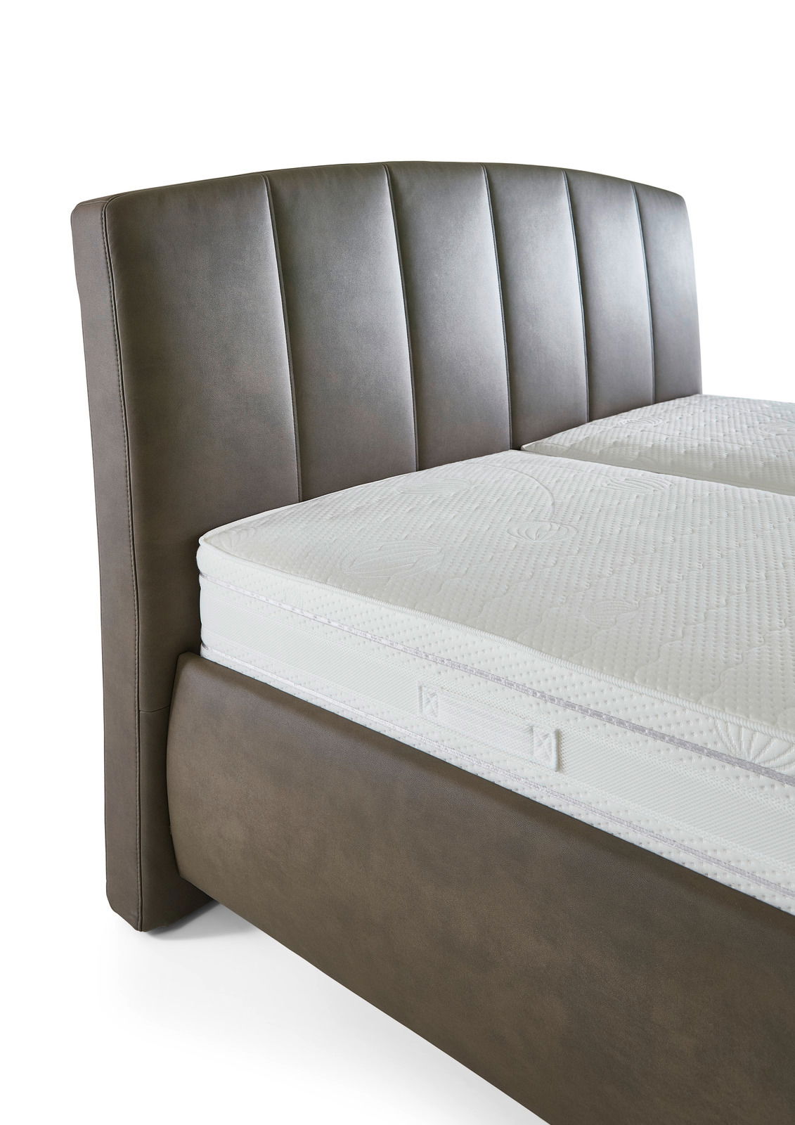 Nahaufnahme eines Polsterbetts mit braunem Kopfteil und weißer Matratze, seitliche Perspektive