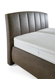 Nahaufnahme eines Polsterbetts mit braunem Kopfteil und weißer Matratze, seitliche Perspektive