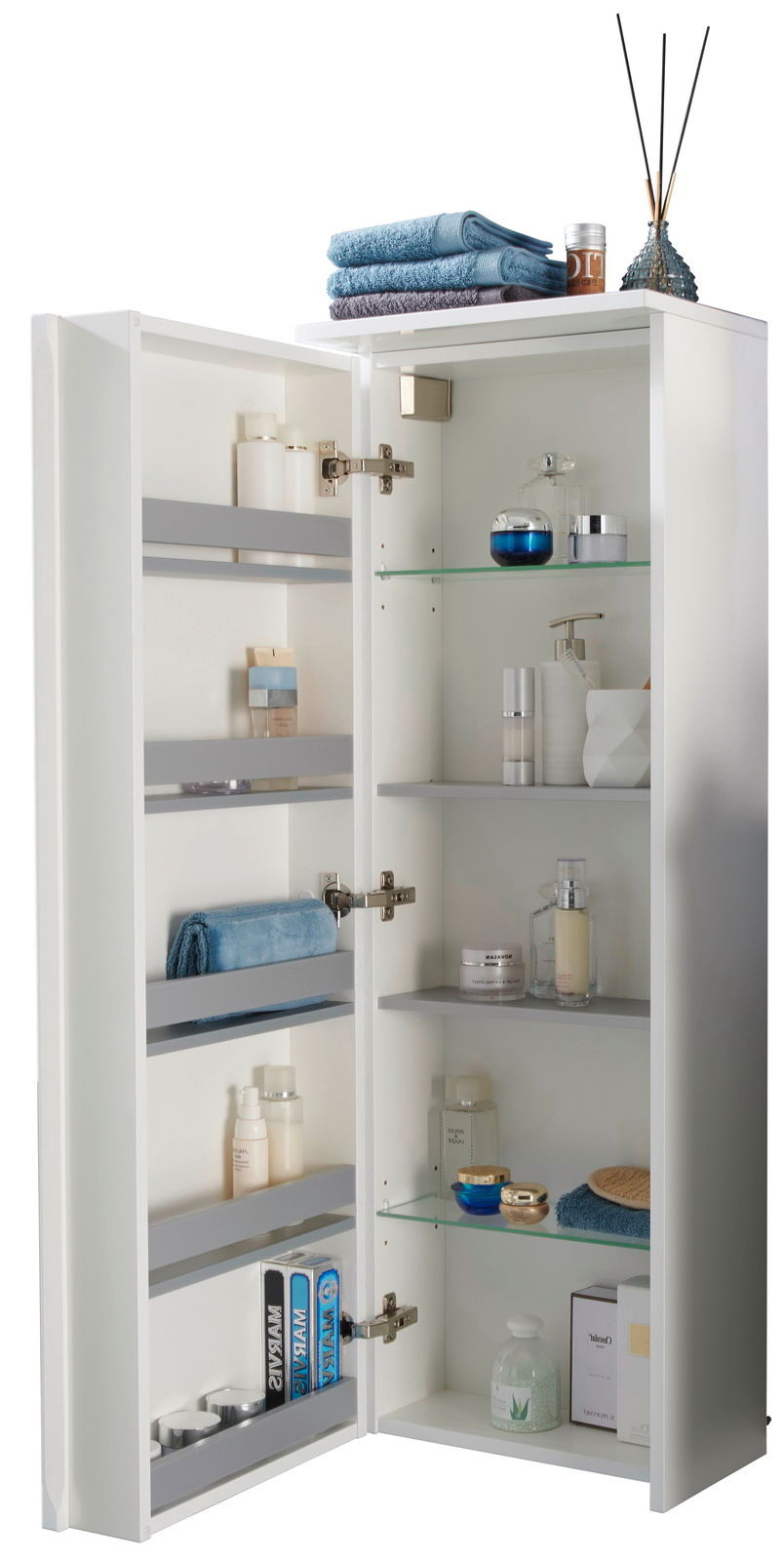 Geöffneter Kofferschrank links mit mehreren Regalen, gefüllt mit Handtüchern, Pflegeprodukten und Dekorationen, aus einer leicht seitlichen Perspektive fotografiert.