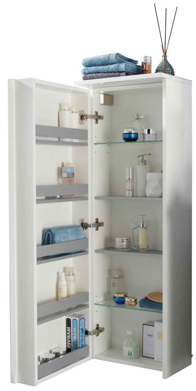 Geöffneter Kofferschrank links mit mehreren Regalen, gefüllt mit Handtüchern, Pflegeprodukten und Dekorationen, aus einer leicht seitlichen Perspektive fotografiert.