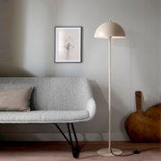 Beige Stehlampe mit halbkugelförmigem Schirm und rundem Standfuß neben grauem Sofa in modernem Wohnzimmer, Frontansicht auf Augenhöhe.