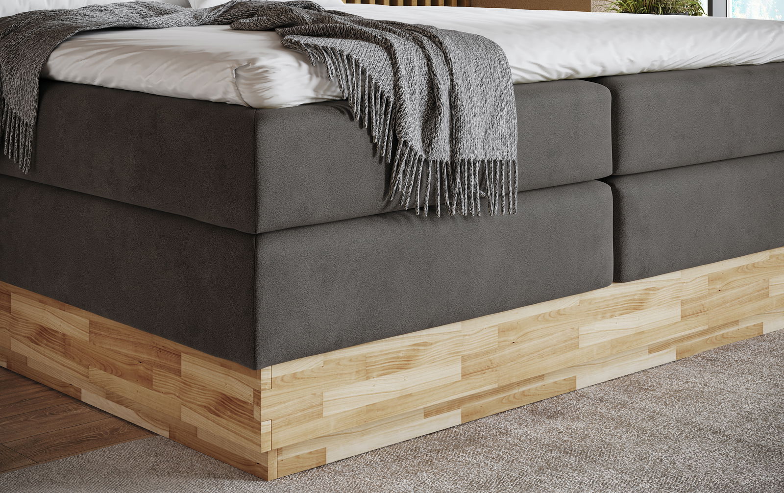 Nahaufnahme eines modernen Boxspringbetts mit grauem Stoffbezug und Holzunterbau, seitliche Perspektive.