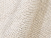 Nahaufnahme eines handgewebten Teppichs in cremeweißer Farbe mit sichtbarer Textur und Falten.