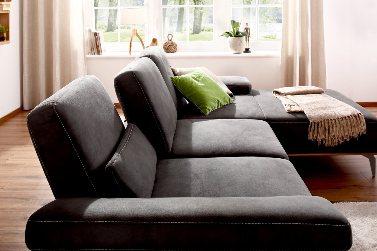 Grijze longchair-set Valnatura 16580 SPRINT in een lichte ruimte met houten vloer, gezien vanaf de zijkant, versierd met groene en beige kussens en een deken.