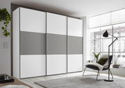 Moderner Schwebetürenschrank in Weiß und Grau, seitliche Perspektive, in einem hellen Raum mit großen Fenstern.