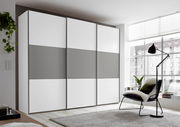 Moderner Schwebetürenschrank in Weiß und Grau, seitliche Perspektive, in einem hellen Raum mit großen Fenstern.