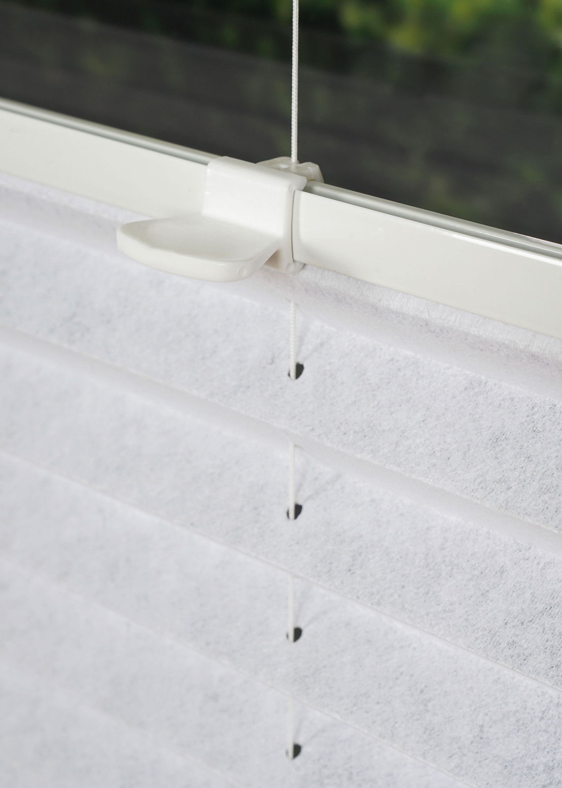Nahaufnahme eines weißen, gefädelten Plissees an einem Fensterrahmen, seitliche Perspektive