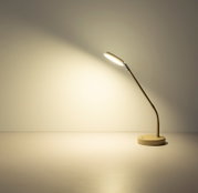 Moderne LED-Schreibtischlampe in Weiß mit rundem Standfuß und flexiblem Metallarm, eingeschaltet und nach links gerichtet, Seitenansicht auf einem hellen Tisch vor neutraler Wand