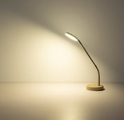Moderne LED-Schreibtischlampe in Weiß mit rundem Standfuß und flexiblem Metallarm, eingeschaltet und nach links gerichtet, Seitenansicht auf einem hellen Tisch vor neutraler Wand