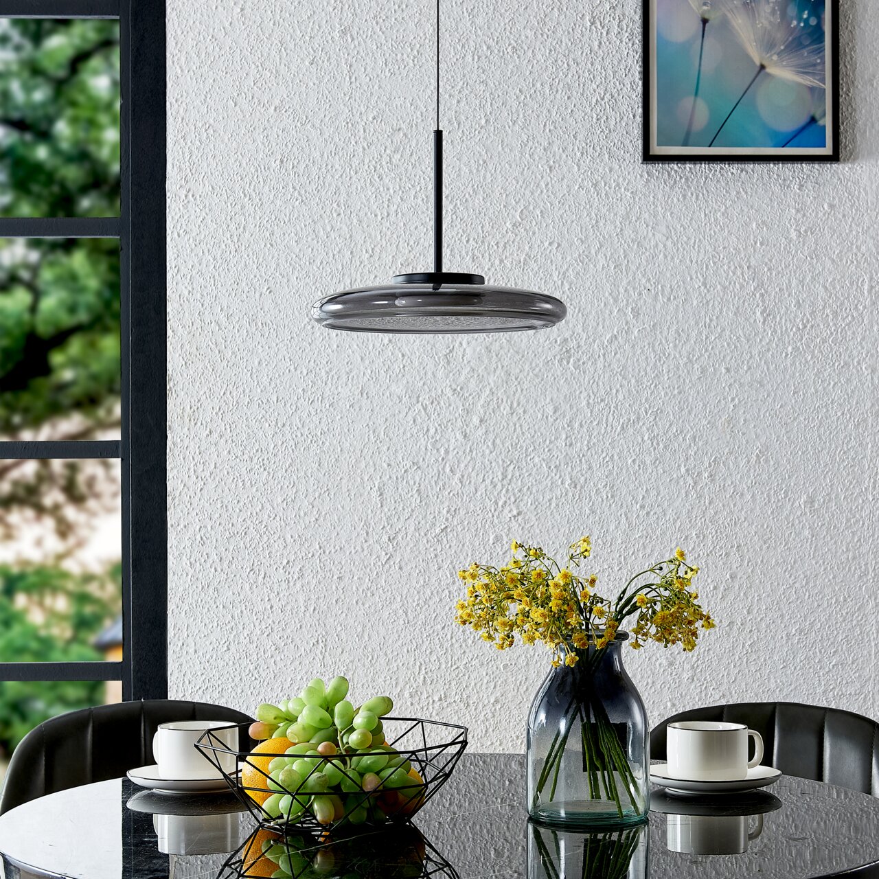 Moderne LED-Hängeleuchte in einem Esszimmer, von der Seite betrachtet, über einem Tisch mit Blumen und Obstkorb.