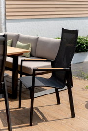 Moderner schwarzer Stapelsessel mit Netzbespannung und Holzarmlehnen auf einer Terrasse, seitliche Perspektive.