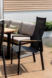 Moderner schwarzer Stapelsessel mit Netzbespannung und Holzarmlehnen auf einer Terrasse, seitliche Perspektive.