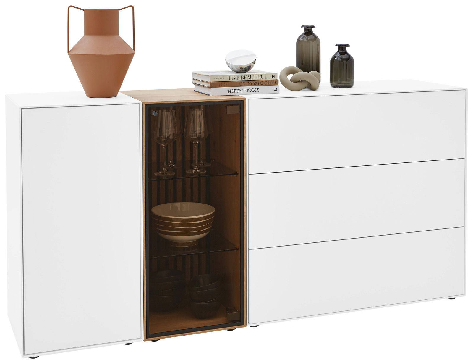 Weißes Sideboard mit drei Schubladen und einem offenen Fach mit Glastür, dekoriert mit Vasen und Büchern, Frontalansicht.