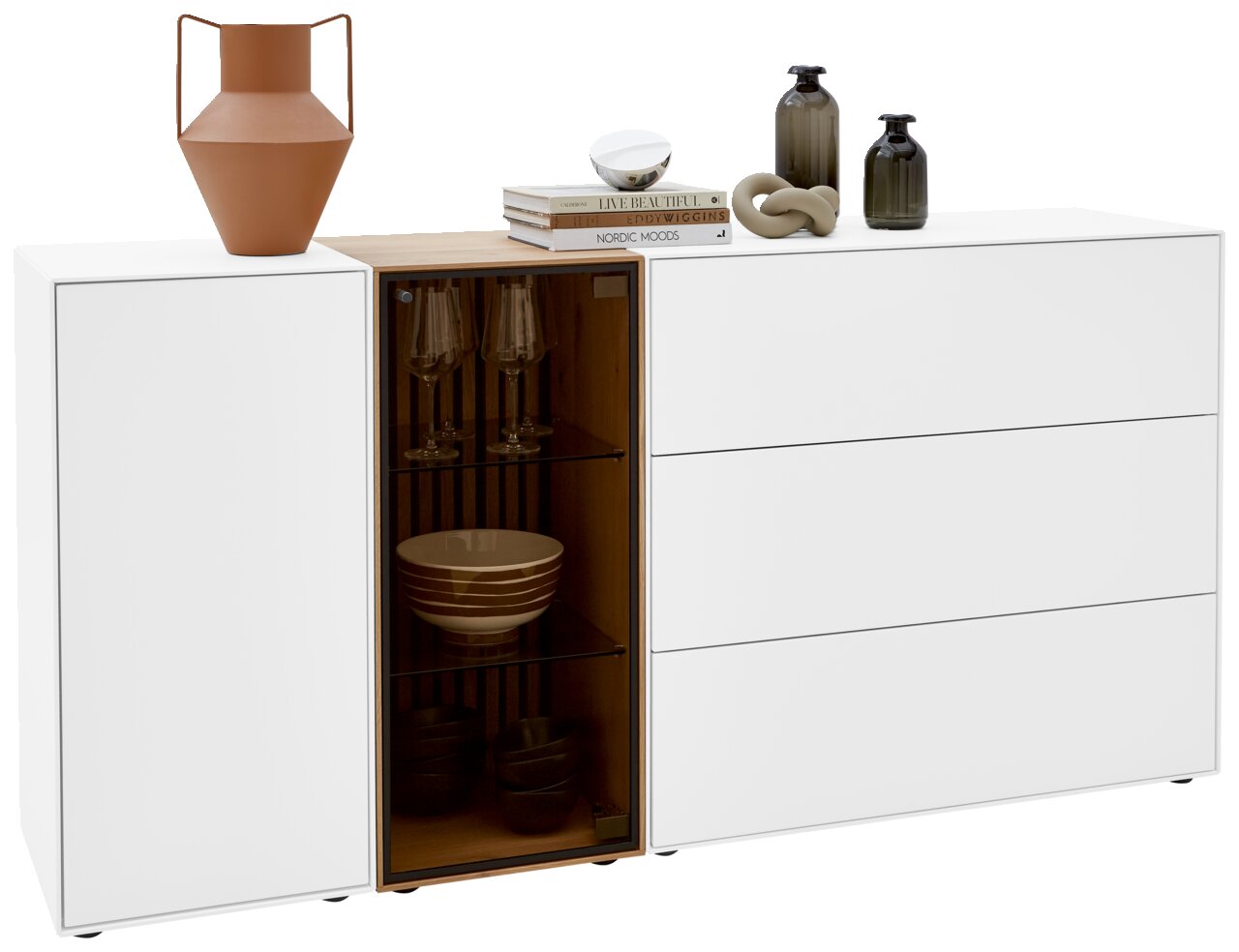 Wit dressoir met drie lades en een open vak met glazen deur, versierd met vazen en boeken, gezien van voren.