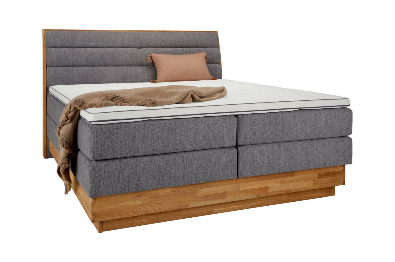 Boxspringbett mit grauem Stoffbezug, Holzrahmen und Kopfteil, seitliche Perspektive