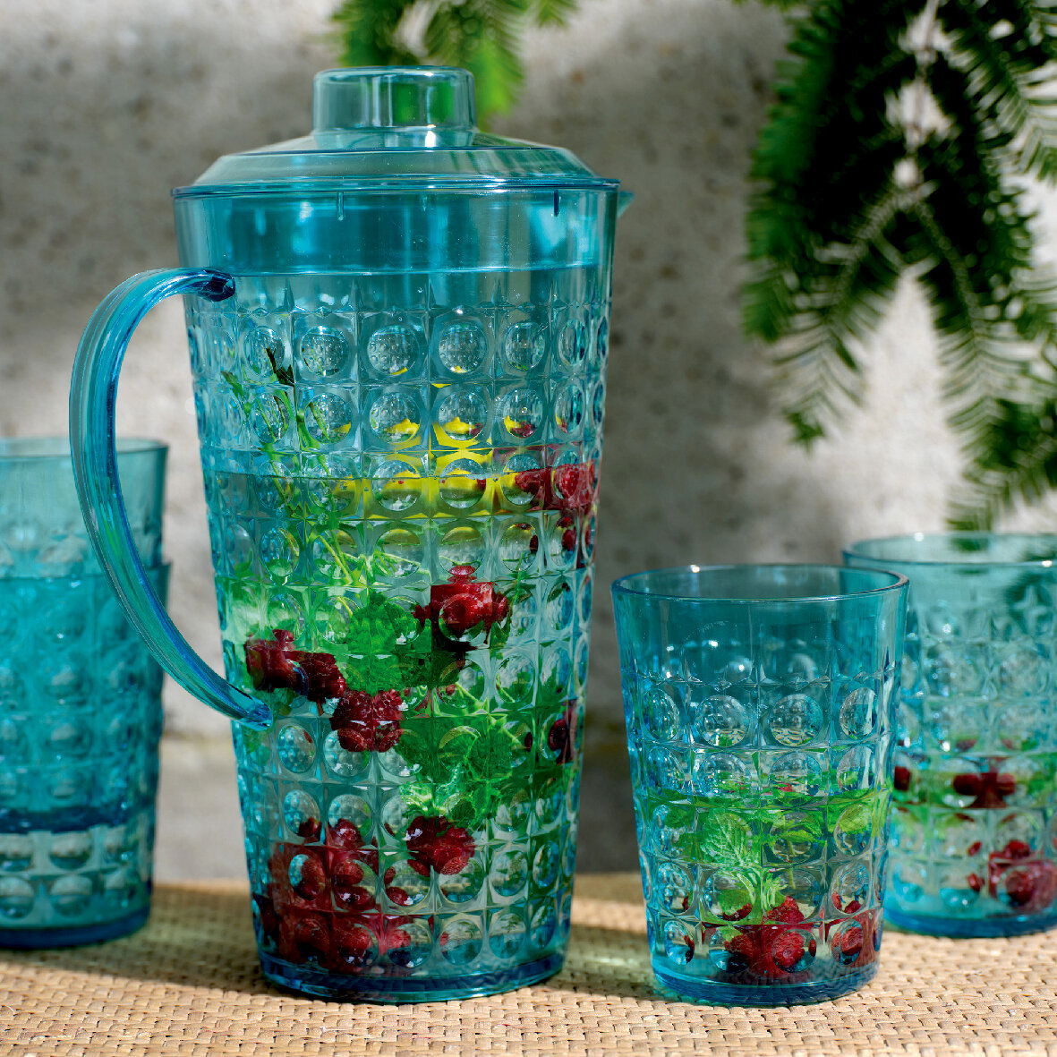 Blaues Kannenset mit Beeren und Minze, von vorne fotografiert, auf einem Tisch im Freien.