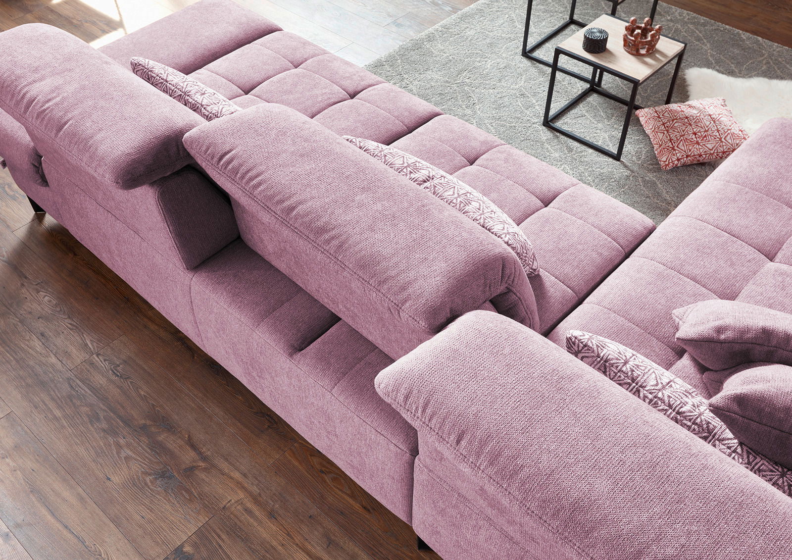 Lila Ecksofa mit klappbaren Armlehnen und dekorativen Kissen, von oben betrachtet.