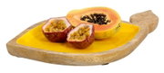Servierschale aus Mangoholz in Blattform mit gelber Innenfläche, darauf frische Früchte wie Papaya und Passionsfrucht, seitliche Perspektive.