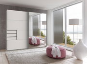 Moderner Schwebetürenschrank mit Spiegel in einem hellen Raum mit Blick auf große Fenster und eine gemütliche Sitzgelegenheit, seitliche Perspektive.