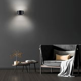 Moderne Wandleuchte PURE CLIPSE in schwarzem Design, an einer dunklen Wand montiert, mit indirekter Beleuchtung nach oben und unten, im stilvollen Wohnzimmerambiente.