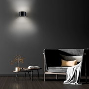 Moderne wandlamp PURE CLIPSE in zwart, gemonteerd op een donkere muur, met indirecte verlichting naar boven en beneden, in een stijlvolle woonkamer.