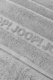 Nahaufnahme eines grauen, flauschigen Frottee-Handtuchs mit eingewebtem Schriftzug „JOOP!“ in schräger Draufsicht.