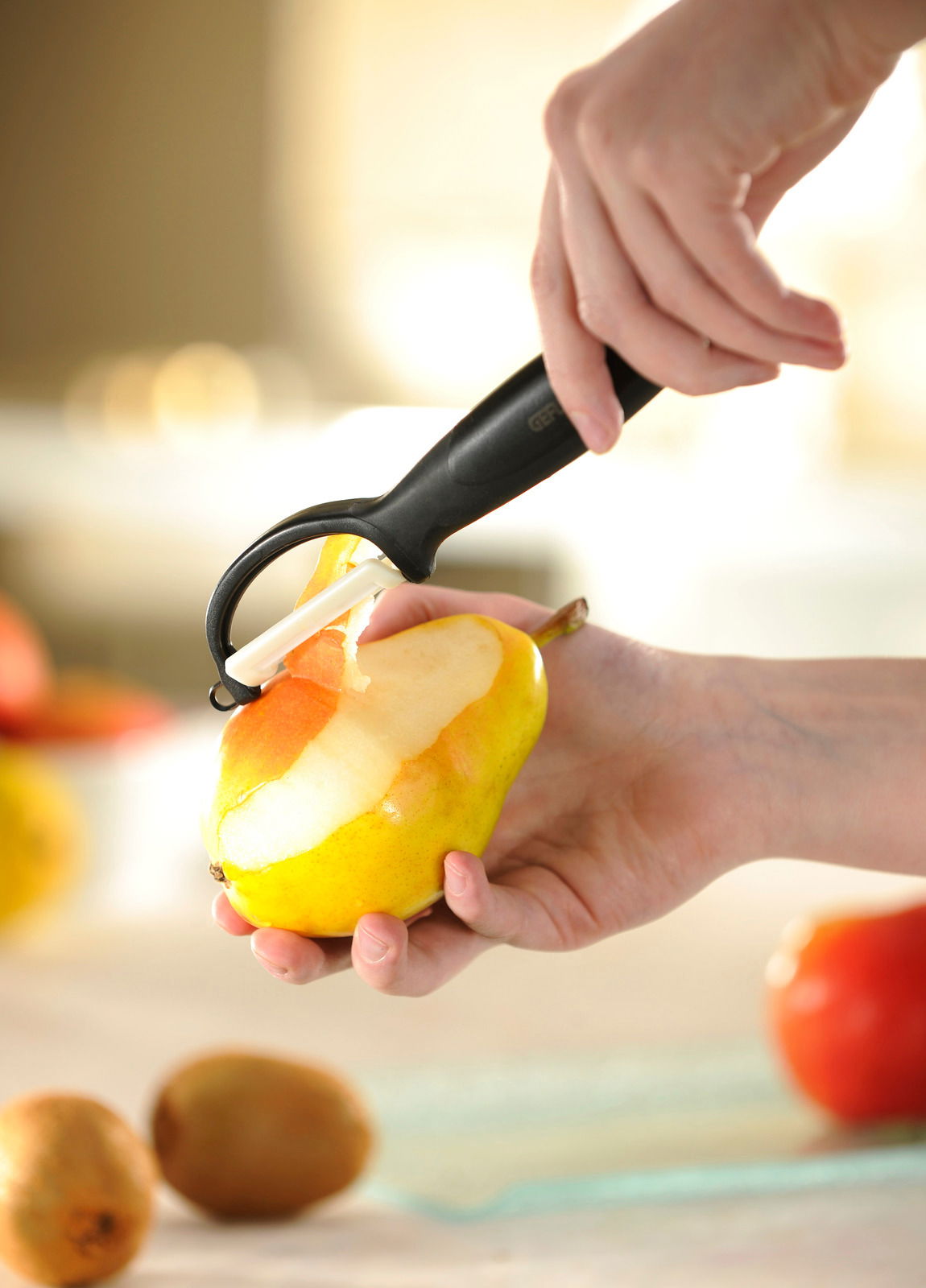 Nahaufnahme eines Keramik-Sparschälers, der eine Birne schält, mit Fokus auf die Klinge und die Schälbewegung.