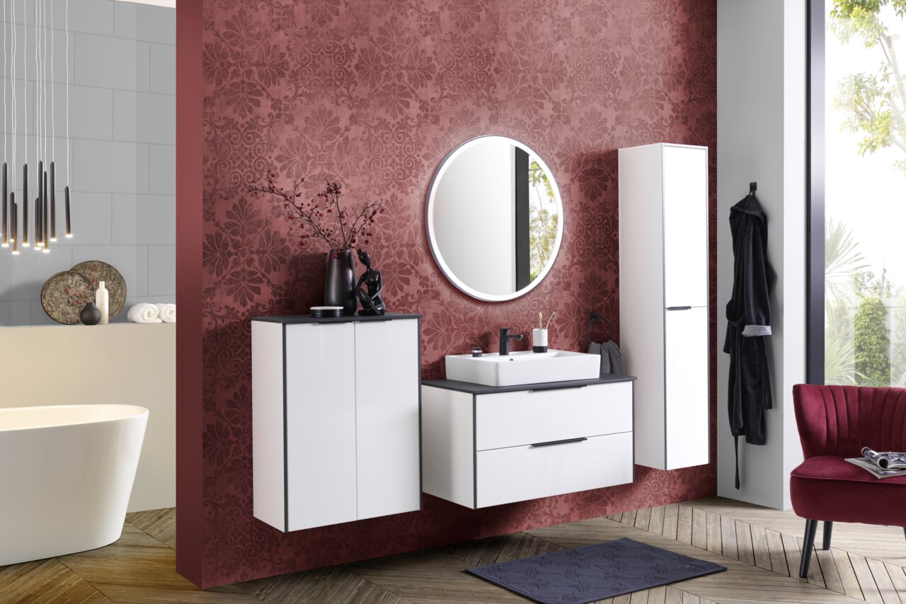 Modernes Waschtisch-Set in einem stilvollen Badezimmer mit roter Akzentwand, rundem Spiegel und eleganten weißen Schränken, aus der Perspektive von vorne betrachtet.