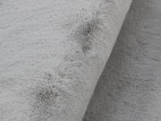 Nahaufnahme eines grauen Fellteppichs mit weicher, flauschiger Textur, seitliche Perspektive