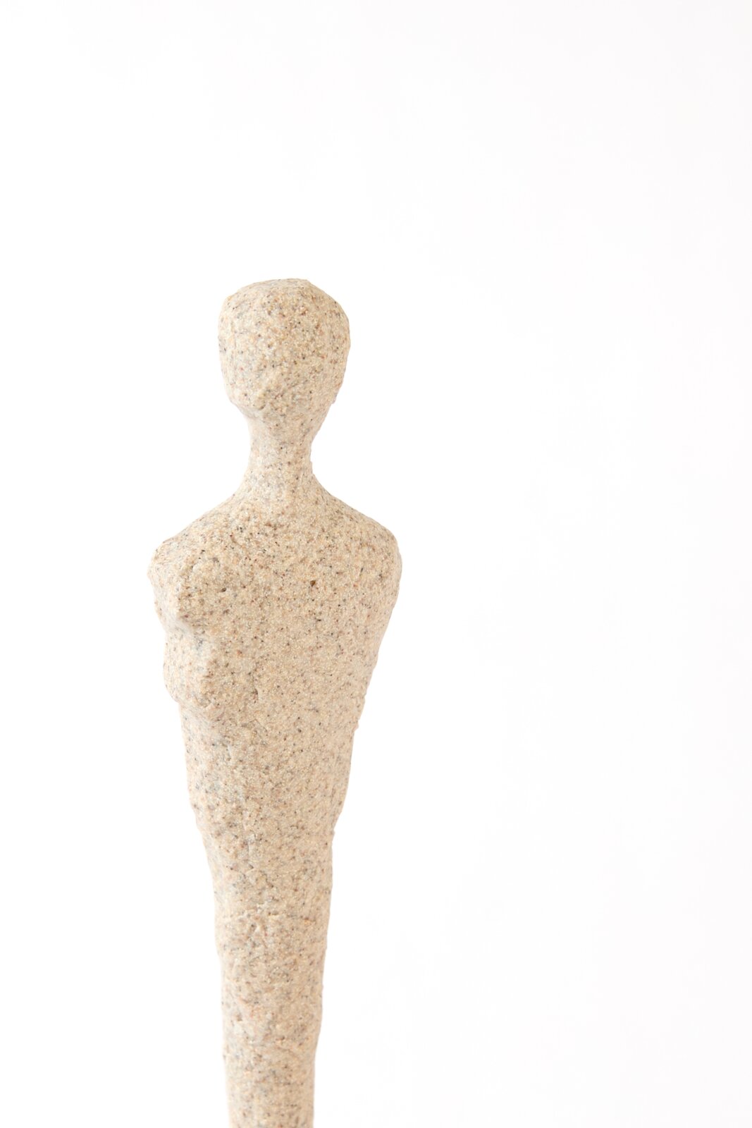 Abstract beige sculptuur van een slanke menselijke figuur met een ruwe, gespikkelde steenachtige textuur, recht van voren afgebeeld tegen een witte achtergrond
