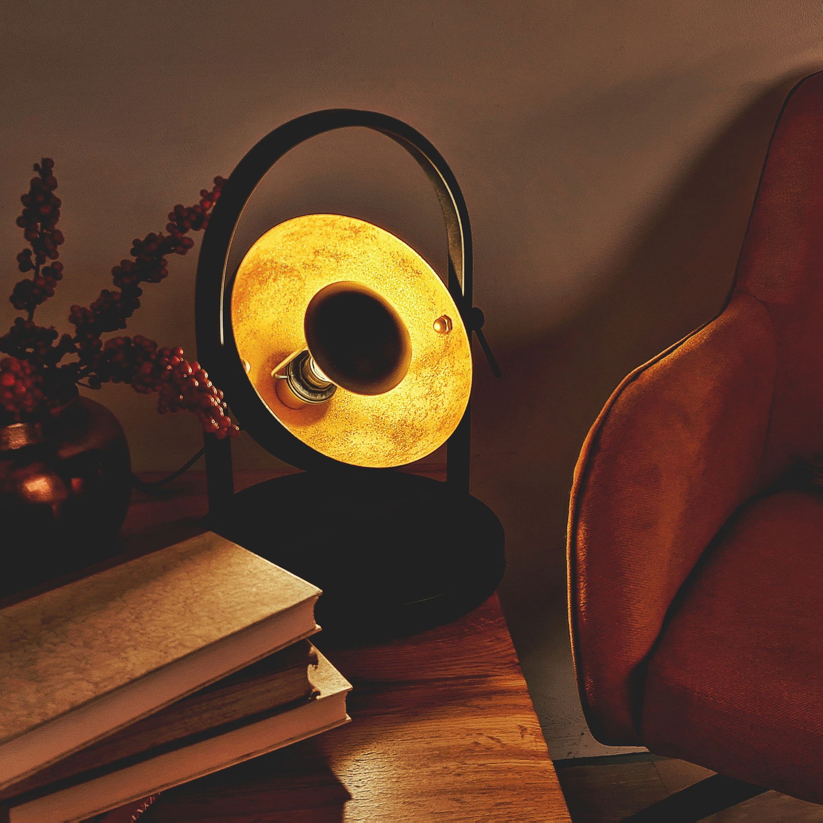 Tischleuchte OLE in einem gemütlichen Wohnzimmer, seitliche Perspektive, warmes Licht, neben einem Sessel und Büchern auf einem Holztisch.