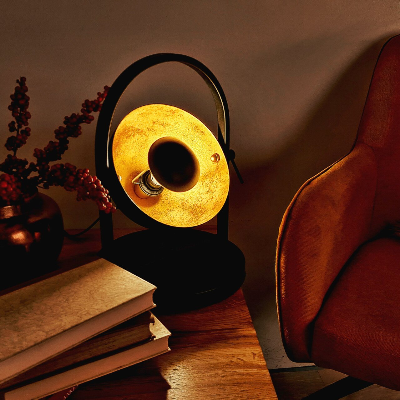Tischleuchte OLE in einem gemütlichen Wohnzimmer, seitliche Perspektive, warmes Licht, neben einem Sessel und Büchern auf einem Holztisch.
