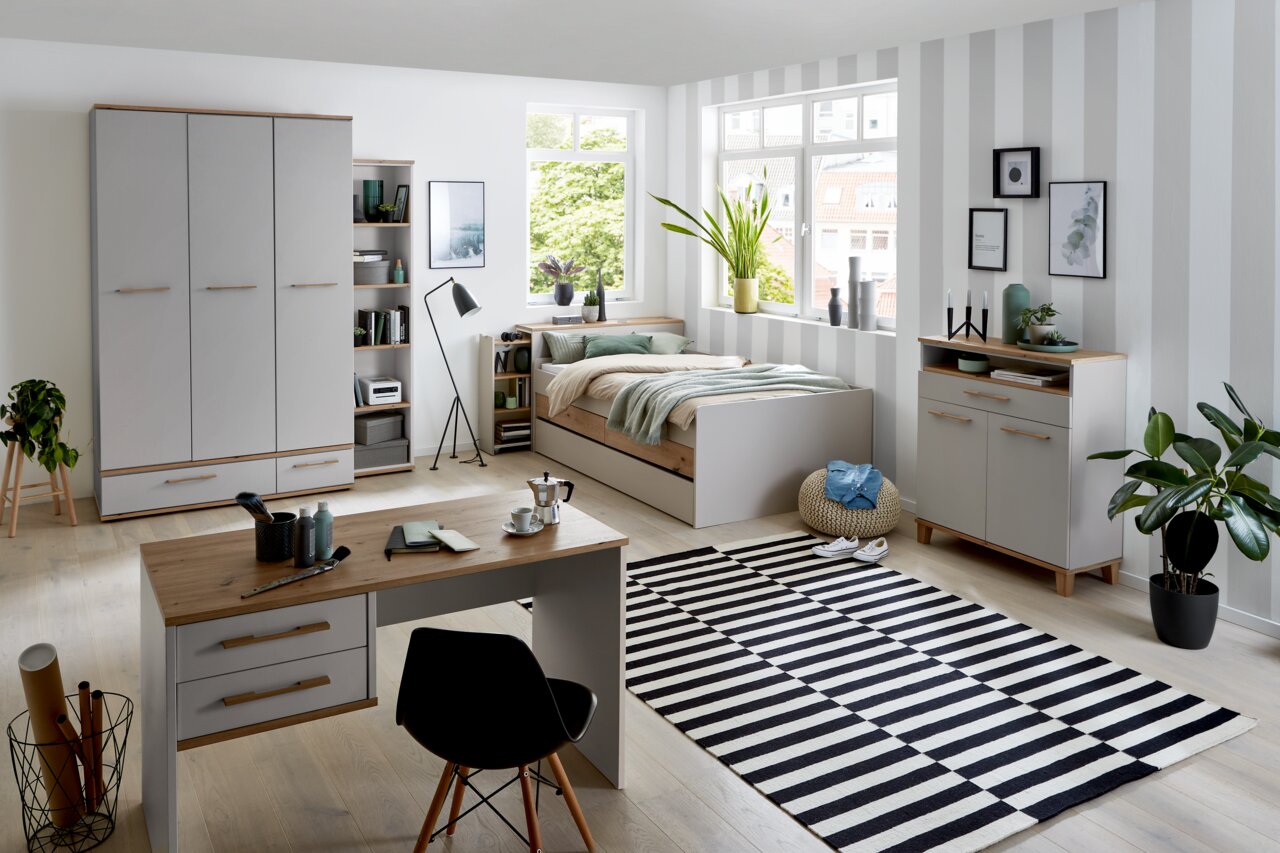 Modernes Jugendzimmer mit Drehtürenschrank, Schreibtisch, Bett und Regalen in heller, freundlicher Atmosphäre. Perspektive: Frontalansicht des gesamten Zimmers.