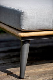 Nahaufnahme eines Loungemöbels mit grauem Kissen, Holzrahmen und Metallbein, seitliche Perspektive