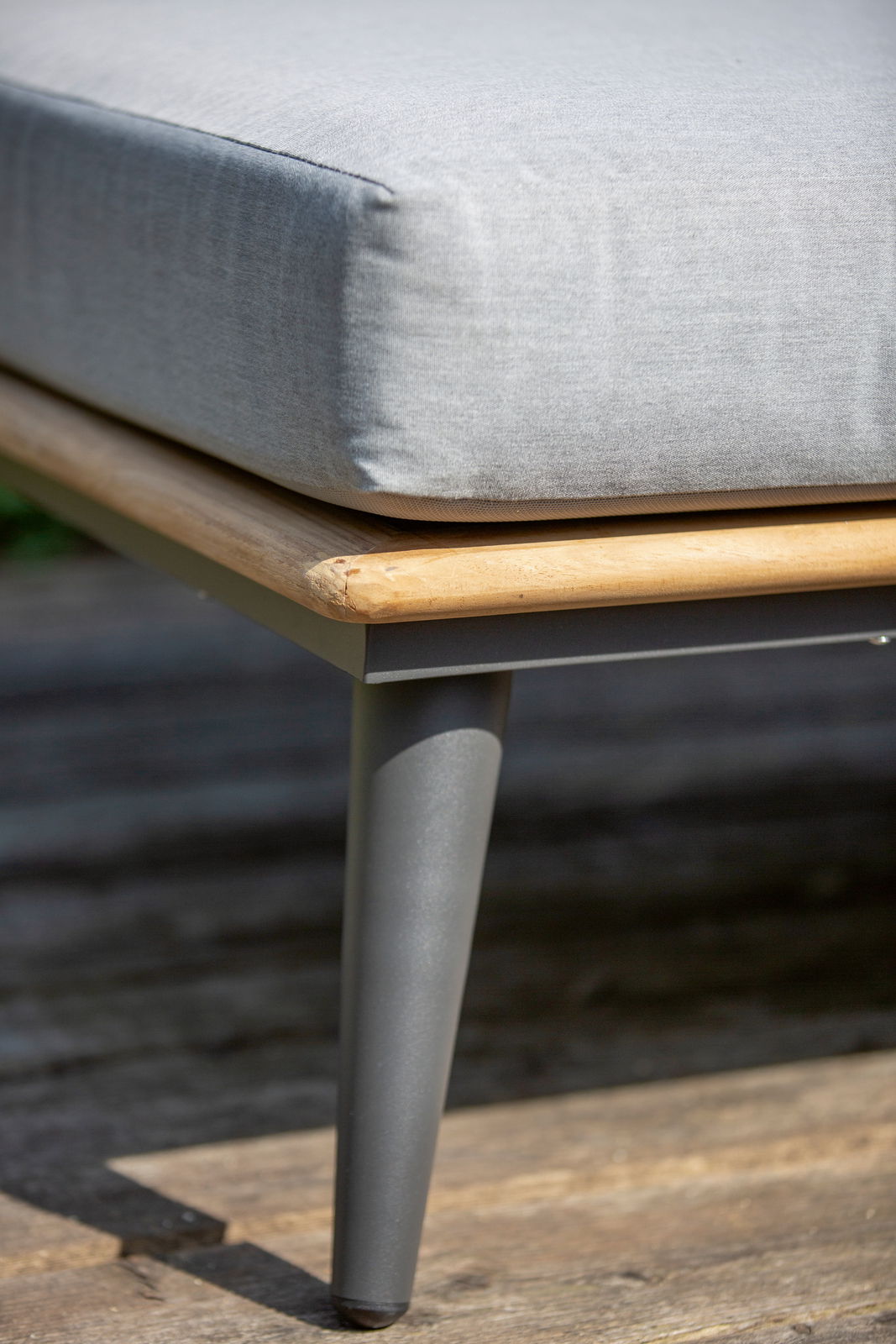 Nahaufnahme eines Loungemöbels mit grauem Kissen, Holzrahmen und Metallbein, seitliche Perspektive