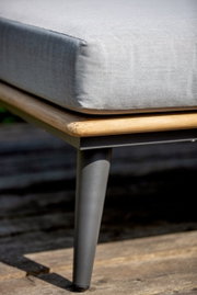 Nahaufnahme eines Loungemöbels mit grauem Kissen, Holzrahmen und Metallbein, seitliche Perspektive